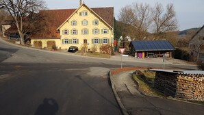 Un edifici groc amb teulada vermella, un cotxe negre estacionat al davant i una estructura de panell solar a prop.