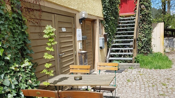 Un pati amb taula i cadires de fusta, una porta vermella i una escala que mena a un segon pis.