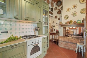 Une cuisine avec des meubles de couleur verte, une cuisinière blanche et une cheminée en briques.