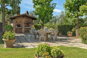 Une terrasse en pierre avec une cheminée en briques, des meubles d’extérieur et des plantes en pot.