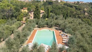Piscina rodeada por oliveiras e uma encosta com edifícios.