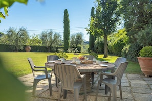 Een terras met een ronde tafel en stoelen, omringd door een tuin met diverse planten en bomen.