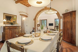 Een eethoek met een lange tafel gedekt voor een maaltijd, houten stoelen, een kroonluchter en een rustieke bakstenen boog.