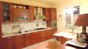 A kitchen with wooden cabinets, a gas stove, a sink, and a dining area with a table and chairs. - CA'LAMBRUSCO App. CRI (4 + 2 PEOPLE) (Smirra di cagli)