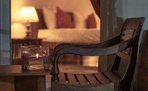 A wooden chair with a glass table beside it, a lit candle, and a bed in the background. - Bohemian Hostel - Negombo (Negombo)