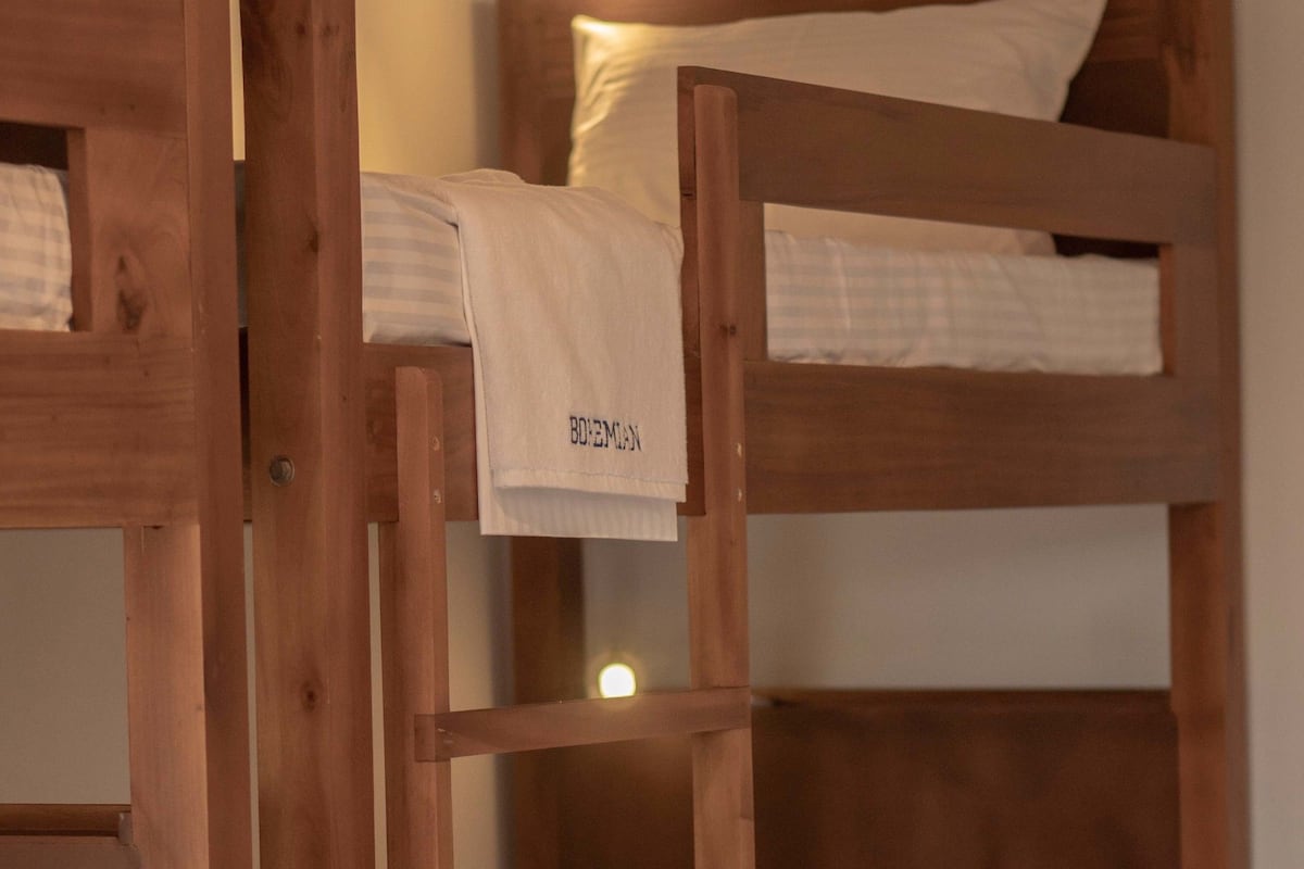 A bunk bed with a wooden frame, white bedding, and a red pillow.
