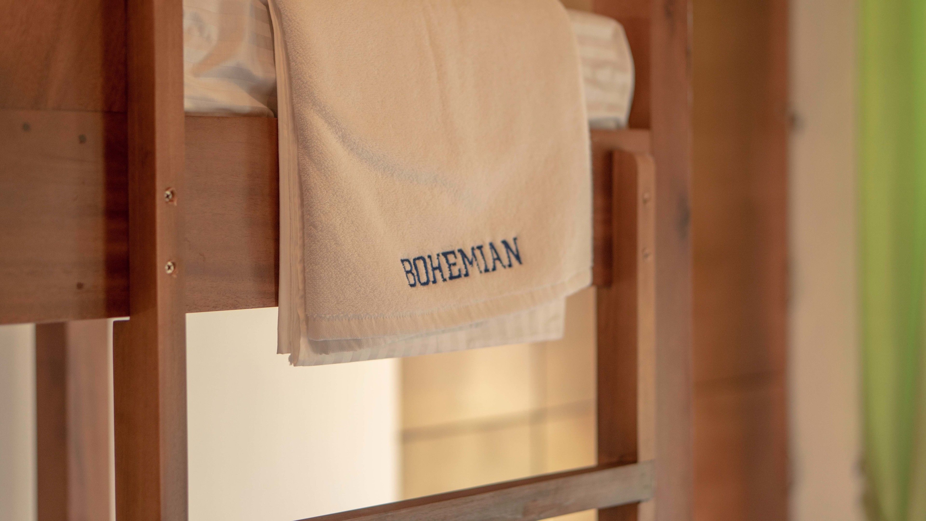 A wooden bed frame with a towel hanging on it that reads "BOHEMIAN".