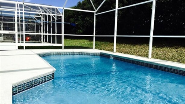 Una piscina con borde de azulejos y un deck blanco que la rodea.