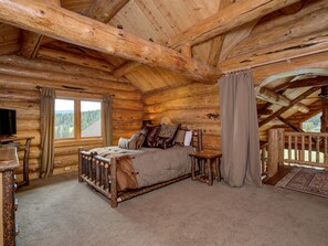 A log cabin bedroom with a bed, a TV, and a window with curtains. - Red Feather Lodge | Luxury Log Cabin for 28 (Big Sky)