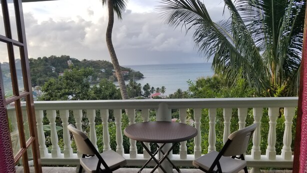 Un balcón con una mesa redonda y dos sillas, con vista a un paisaje costero con palmeras y al mar.