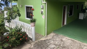 Un edificio verde con un balcón blanco, una planta en maceta con flores rojas y un letrero que dice "WEAR YOUR MASKS".