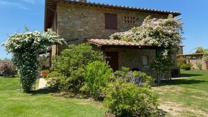 A stone house with a tiled roof, surrounded by lush greenery and flowering bushes. - Desiderio, luxury home with pool AC, WIFI and cook school - A Fontanaro Property (Paciano)