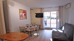A living room with a wooden table, a sofa, a TV mounted on the wall, and a balcony with a chair. - Apartment for 4 people – Air conditioning – WiFi – Downtown – Sainte Maxime (STE MAXIME)