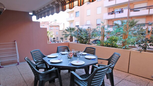 A dining area with a table set for four, surrounded by chairs, on a balcony with a view of a residential building and some greenery. - Apartment for 4 people – Air conditioning – WiFi – Downtown – Sainte Maxime (STE MAXIME)