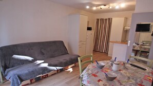 A small, furnished room with a sofa, a table with a floral tablecloth, and a kitchen area in the background. - Apartment for 4 people – Air conditioning – WiFi – Downtown – Sainte Maxime (STE MAXIME)