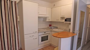A compact kitchen with white cabinets, a microwave, a stove, and a wooden countertop. - Apartment for 4 people – Air conditioning – WiFi – Downtown – Sainte Maxime (STE MAXIME)