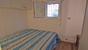 A small, sparsely furnished room with a single bed, a window with bars, and a plain white wall. - Apartment for 4 people – Air conditioning – WiFi – Downtown – Sainte Maxime (STE MAXIME)