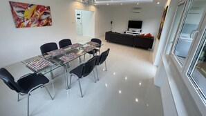 Een moderne eethoek met een glazen tafel en stoelen, een bank en een televisie op de achtergrond.