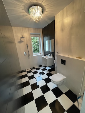 Een badkamer met een zwart-wit geruite vloer, een toilet, een wastafel, een douche en een kroonluchter.