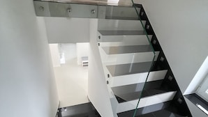 Een moderne trap met glazen balustrades en stappen betegeld met zwart tegels.