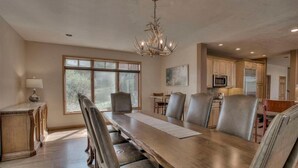 Un comedor espacioso con una larga mesa de madera, sillas de cuero, un candelabro y vista a la cocina al fondo.
