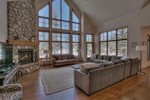 A spacious living room with a stone fireplace, large windows, and a sectional sofa.