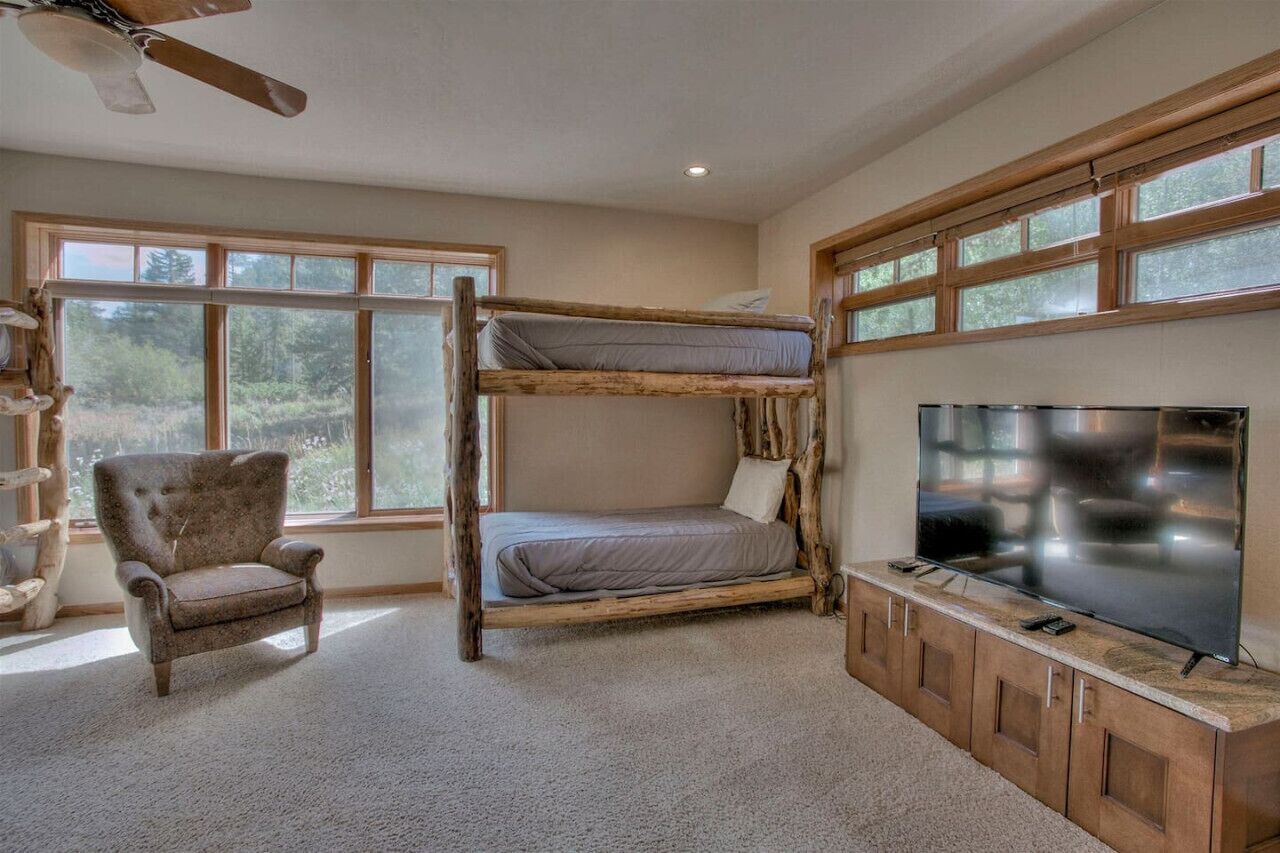 Un lit superposé avec un téléviseur posé sur un meuble en bois, une chaise et de grandes fenêtres.