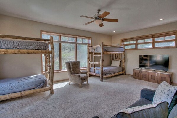 A room with bunk beds, a chair, a sofa, a TV, and a ceiling fan.