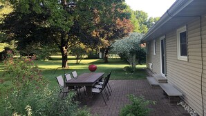 Eine Terrasse mit Tisch und Stühlen, umgeben von Bäumen und einem Rasen.