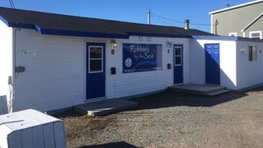 A small, single-story building with a blue door and a sign that reads "Robbins by the Sea." - Robbins by the Sea Rental - Robbins by the Sea 2 unit (Bonavista)