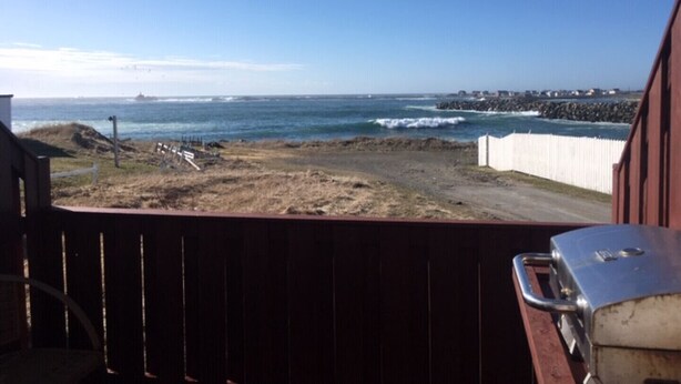 A view from a balcony overlooking a beach with a rocky shoreline and waves crashing against a breakwater. - Robbins by the Sea Rental - Robbins by the Sea 2 unit (Bonavista)