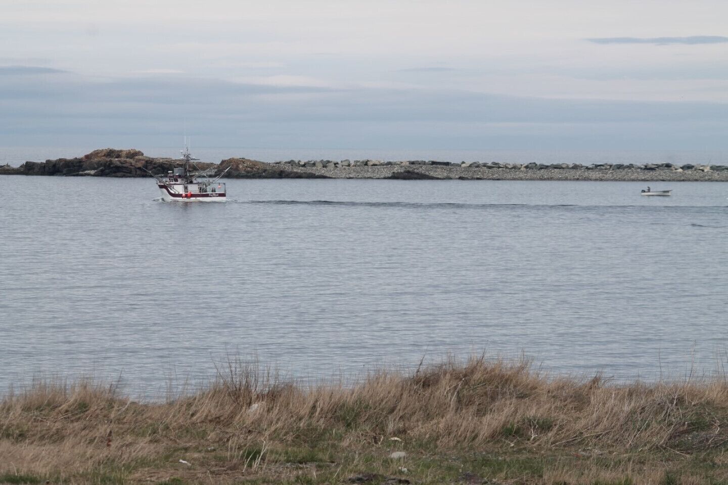 Água calma com um barco pequeno e uma embarcação maior.