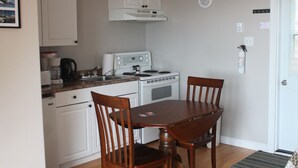 A compact kitchen with white cabinets, a stove, and a dining table with chairs. - Robbins by the Sea Rental - Robbins by the Sea 2 unit (Bonavista)