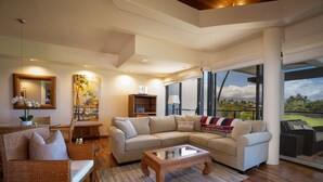 Un salon moderne avec un canapé d’angle, une table basse et une grande fenêtre donnant sur l’extérieur.