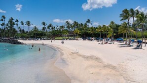 Une plage avec une eau turquoise et limpide, des palmiers, et des gens qui se baignent et prennent des bains de soleil.