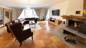 Un salon spacieux doté d’une cheminée, de canapés en cuir, de parquet et d’une grande fenêtre.