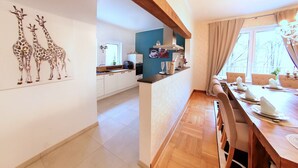 Une cuisine moderne avec des meubles blancs, un plan de travail en bois et un coin repas doté d’une longue table pouvant accueillir six personnes.