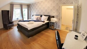 Une chambre moderne avec un grand lit, une chaise, une table de chevet et une vue sur l’extérieur par une fenêtre.