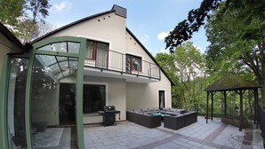 Une maison moderne dotée d’une porte en verre, d’un espace extérieur aménagé pour s’asseoir et d’un patio couvert.