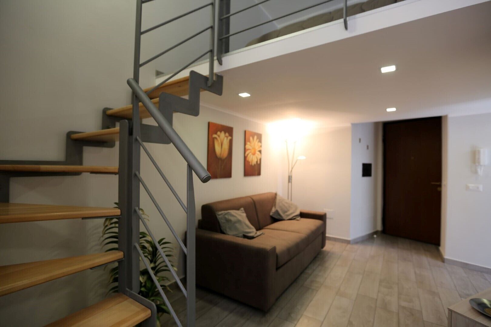 Un salon moderne avec un escalier, un canapé marron et deux tableaux représentant des fleurs, accrochés au mur.