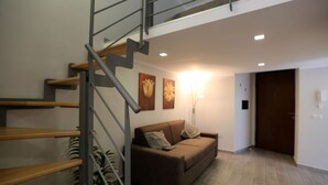 A modern living room with a staircase, a brown sofa, and two wall-mounted flower paintings. - VILLA ROSA - Apartment n. 3 "VIOLA" (4 beds): (Napoli)