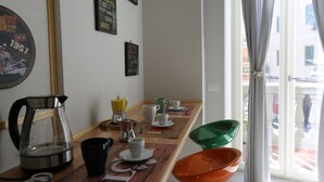 A breakfast table with coffee and tea equipment, a wall with vintage posters, and a view of the street through a window. - VILLA ROSA - Apartment n. 3 "VIOLA" (4 beds): (Napoli)
