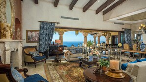 Un vaste salon offrant une vue sur l’océan, agrémenté de meubles anciens, d’un grand tapis et d’une cheminée.