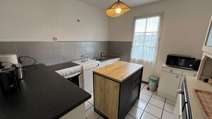 A compact kitchen with a black countertop, a wooden island, a microwave, and a window with blinds. - Ref 006 - Charming Villa in the heart  of the resort (SOULAC SUR MER)