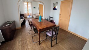 A dining area with a wooden table, chairs, and a blue vase. There is a sofa and a door in the background. - Ref 006 - Charming Villa in the heart  of the resort (SOULAC SUR MER)