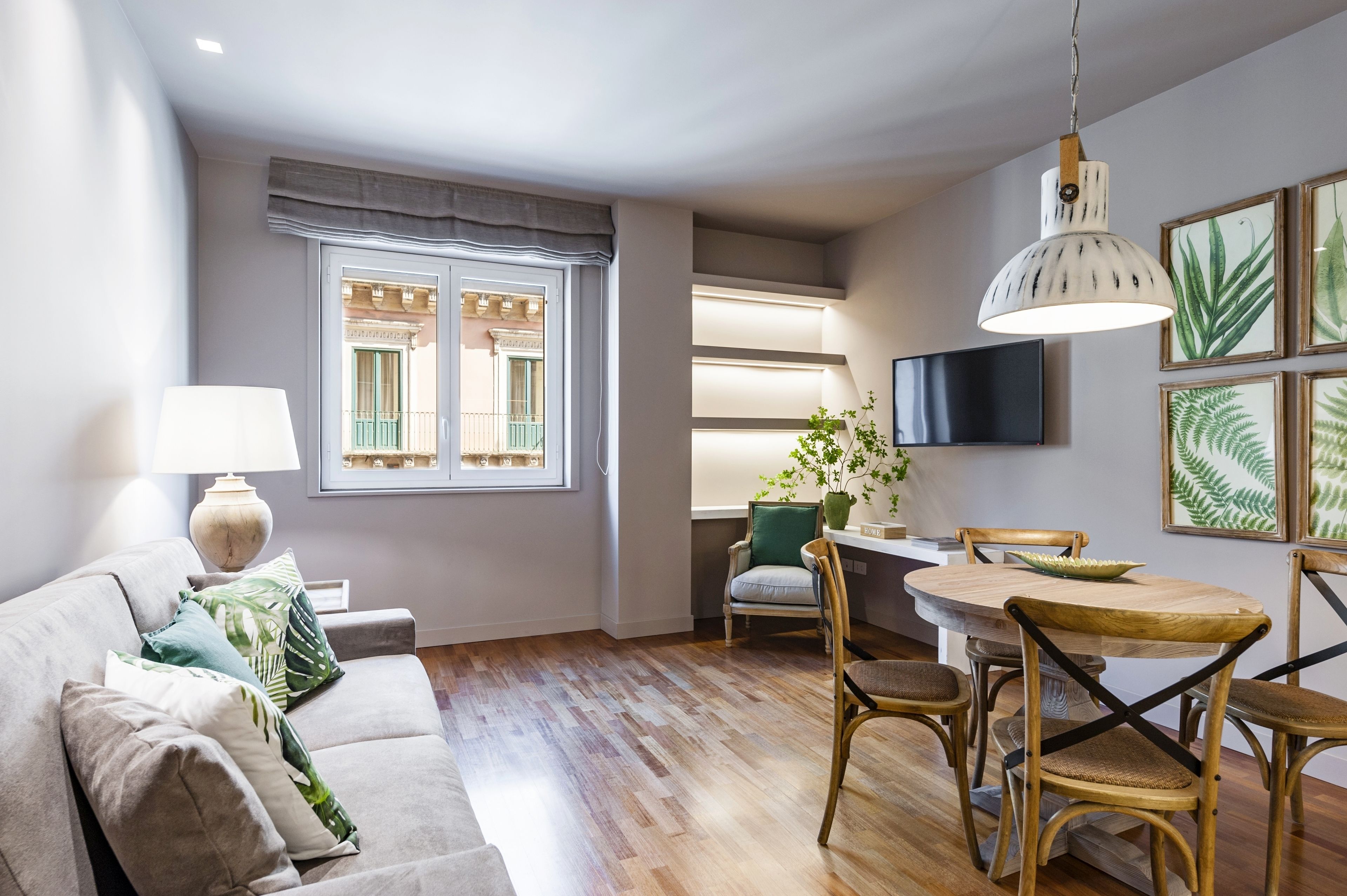 A modern living room with a sofa, a dining table, and chairs. There is a window with a view of buildings outside.