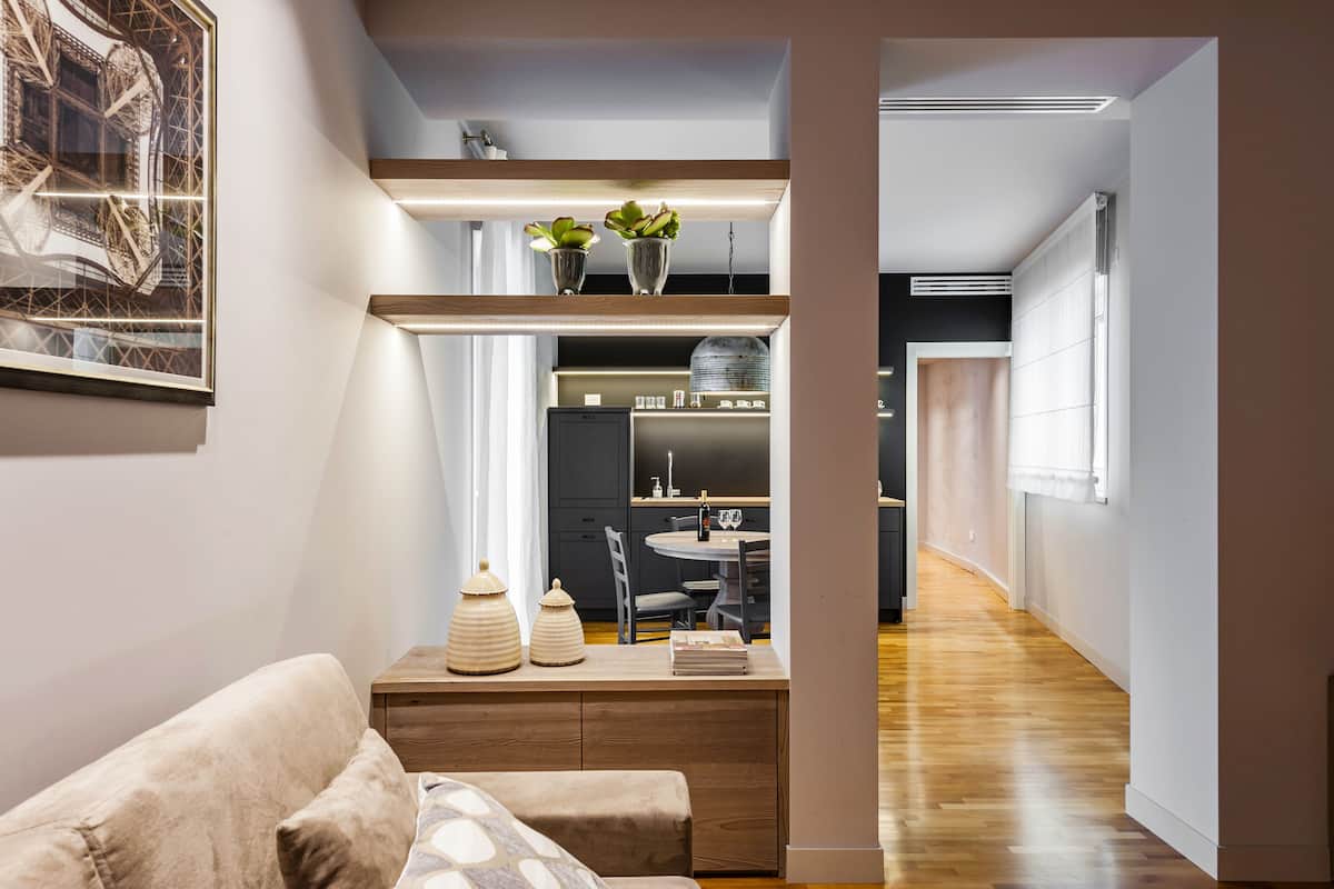 Un interior moderno con un sofá, un área de comedor con mesa y sillas, y una cocina visible a través de un panel de vidrio.