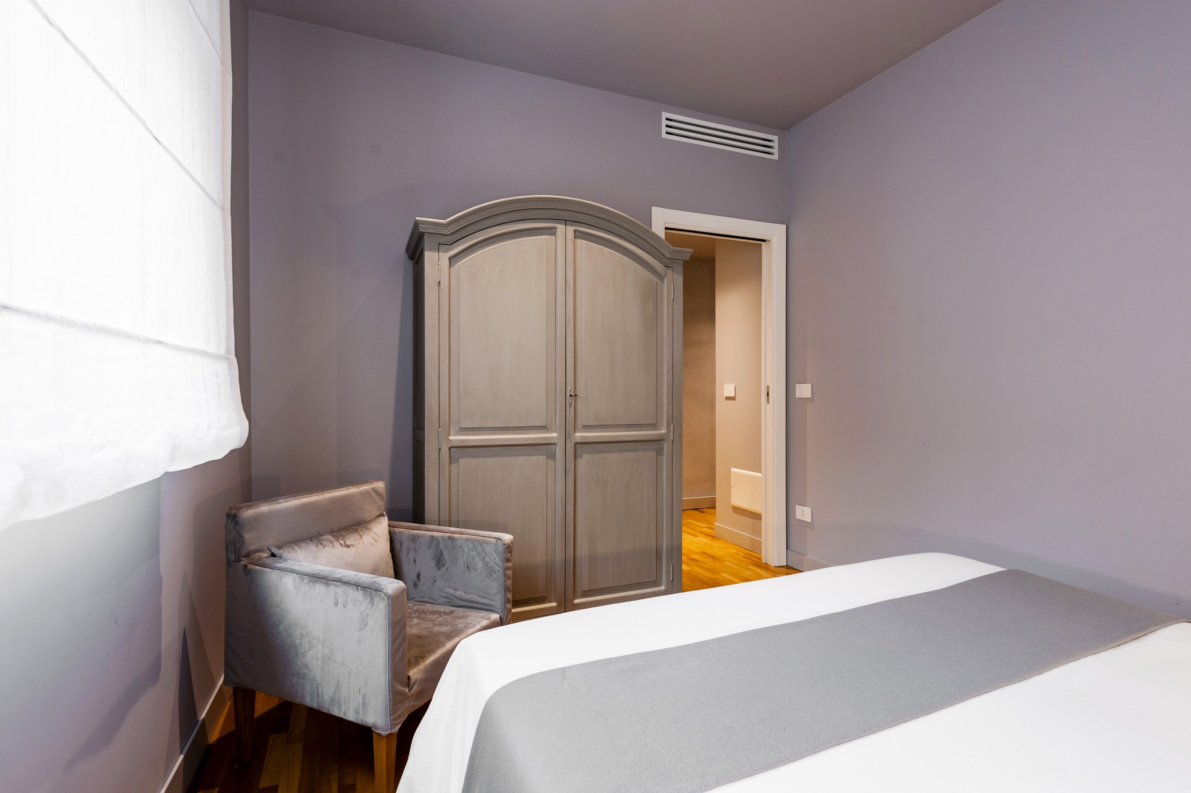 A bedroom with a bed, a wardrobe, and a chair.
