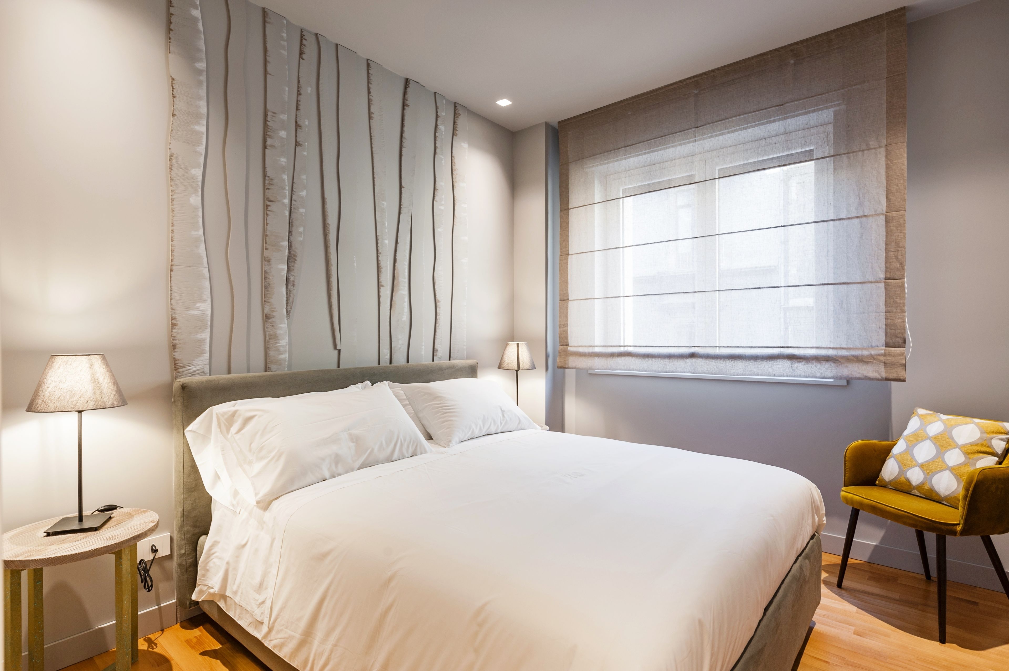 A modern bedroom with a large bed, a nightstand, a lamp, and a chair.