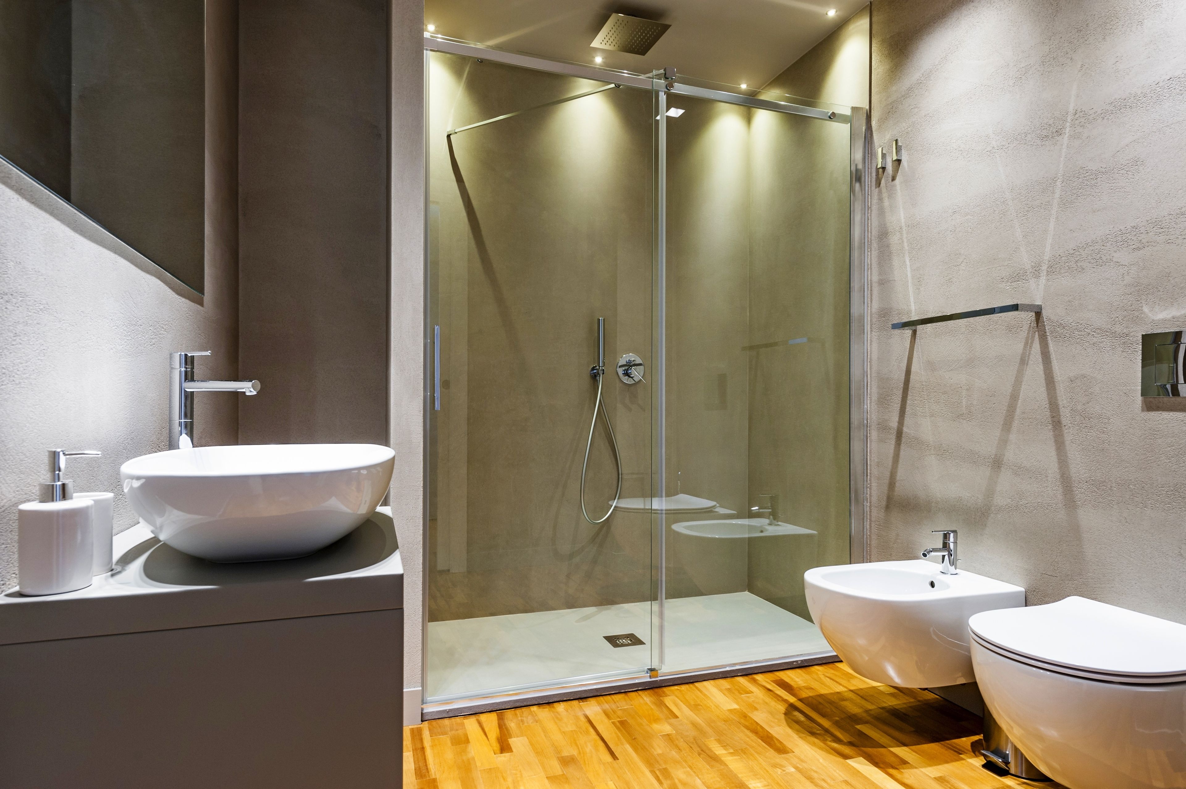 Un baño moderno con ducha envuelta en vidrio, un lavamanos grande tipo recipiente y un lavabo pedestal aparte.